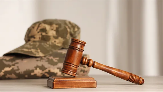 Wooden judge's gavel resting on a block with a camouflage military cap in the background.