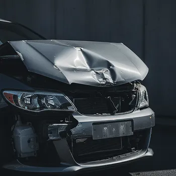 Front view of a dark-colored car with significant hood and bumper damage from a collision.