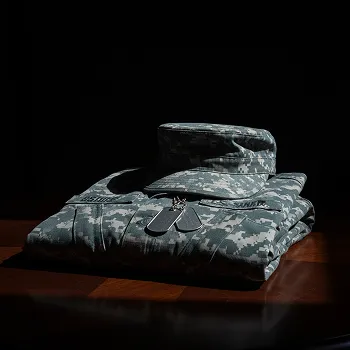 Folded military digital camouflage uniform with matching cap and dog tags on a wooden surface.