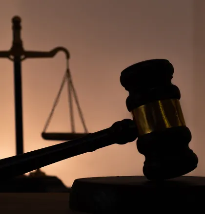 Wooden judge's gavel with brass band in foreground, balanced scales of justice in background.