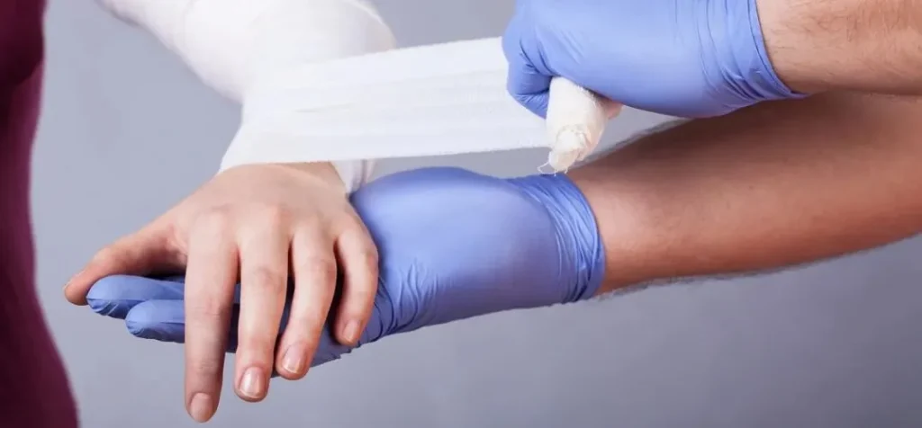 Medical professional wearing blue gloves wrapping a white bandage around a patient's wrist.