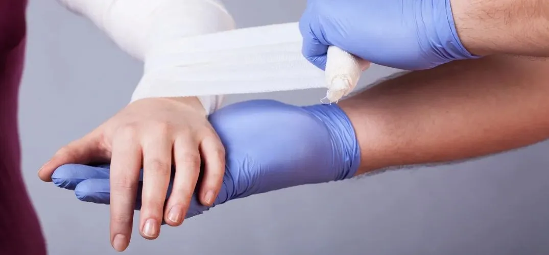 Medical professional wearing blue gloves wrapping a white bandage around a patient's wrist.