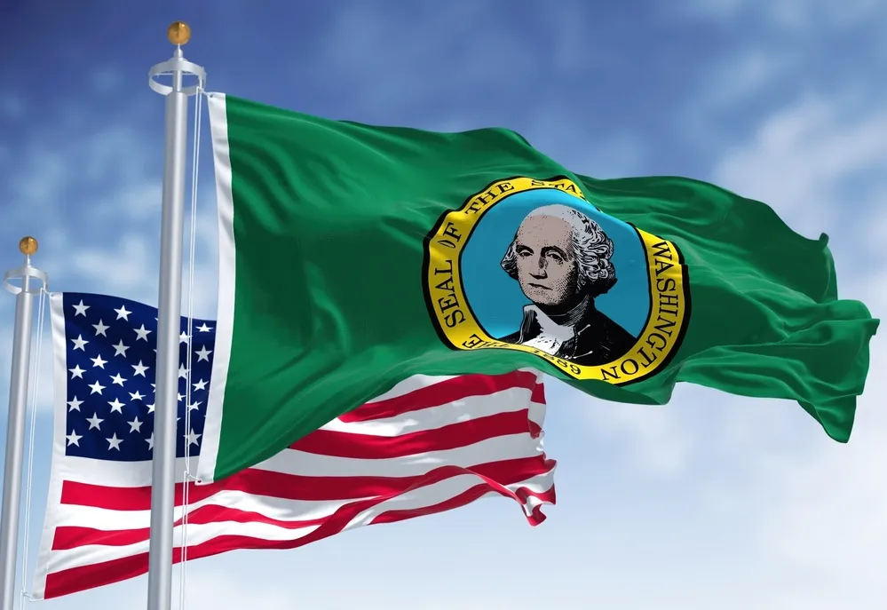 Flags of the United States and Washington state waving against a blue sky.