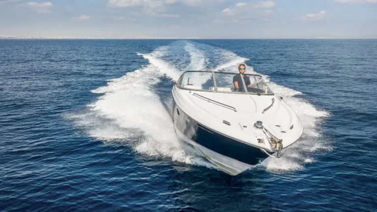 Person steering a white and navy speedboat on calm blue ocean waters under a partly cloudy sky.