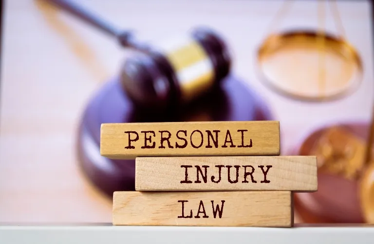 Stacked wooden blocks with the words "PERSONAL INJURY LAW" in front of a judge's gavel and scales of justice.