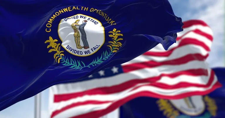 Flag of the Commonwealth of Kentucky with "United We Stand, Divided We Fall" text, American flag in background.