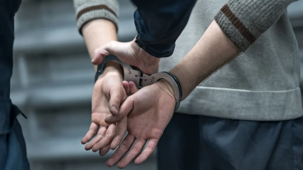 Close-up of a person in a gray sweater being handcuffed behind their back by another individual.